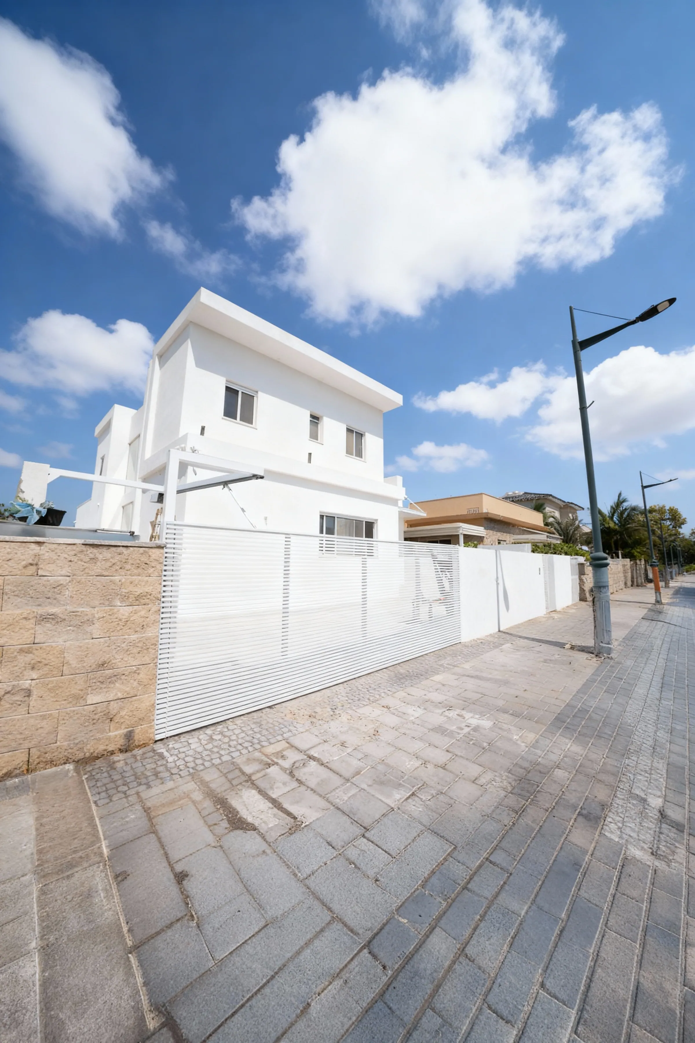 גדר לבנה בשלבים אופקיים לאורך המדרכה, מול וילה לבנה