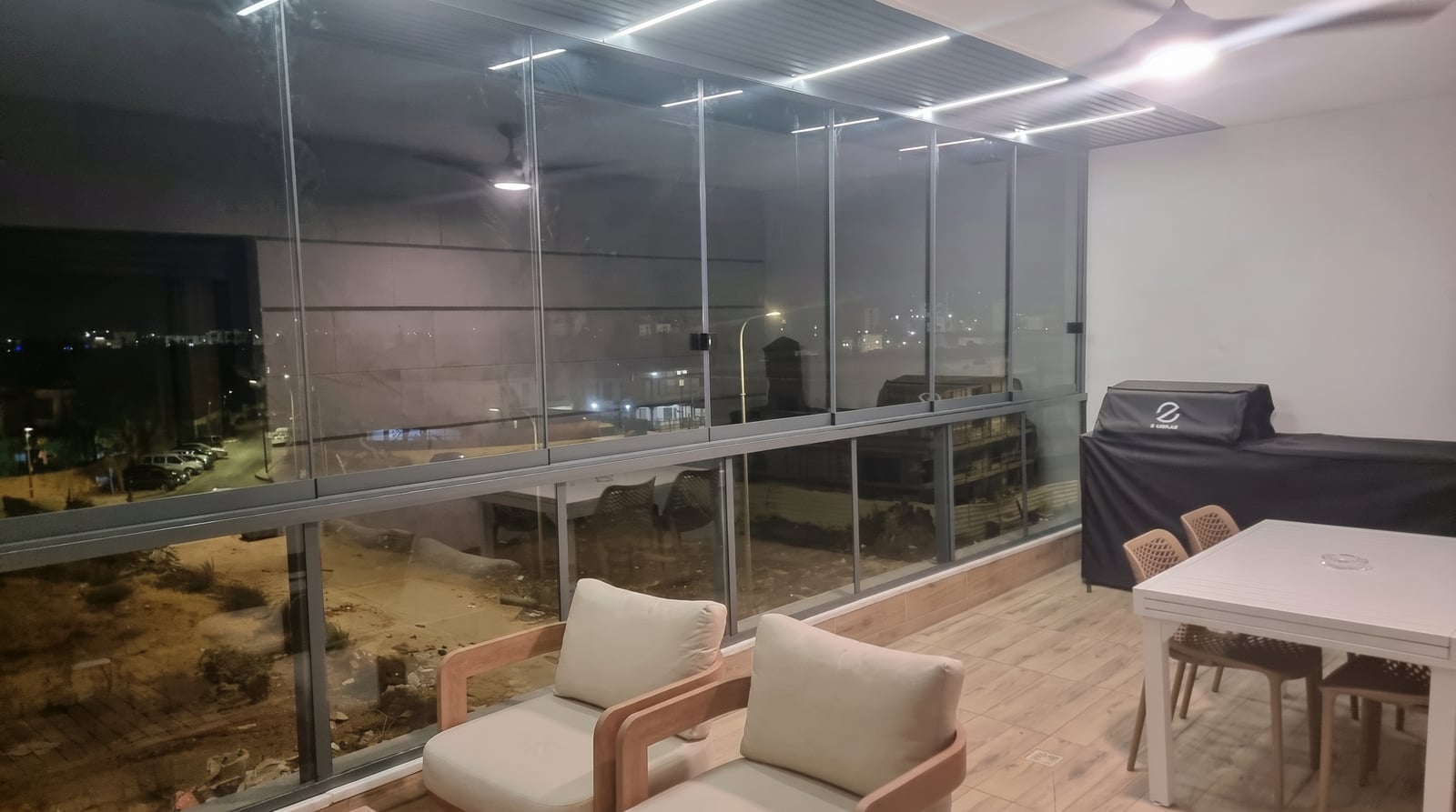 מרפסת סגורה בזכוכית בלילה עם פינת ישיבה, שולחן אוכל ותאורת לד בתקרה