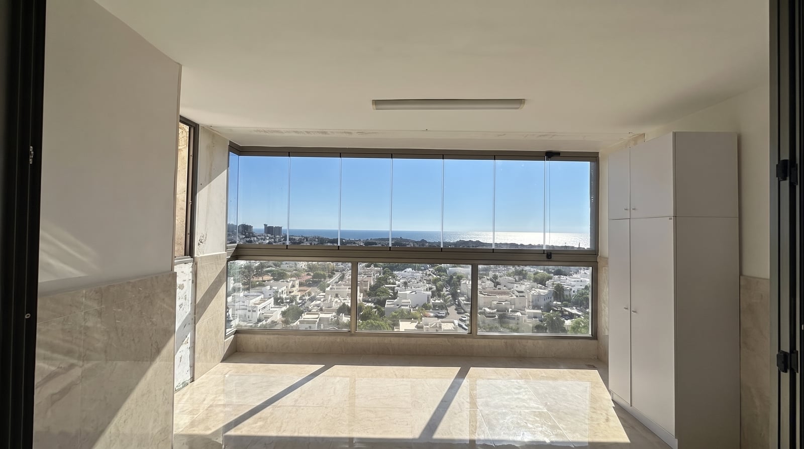 חדר מרפסת סגור בזכוכית עם נוף פתוח לים ולשכונת וילות
