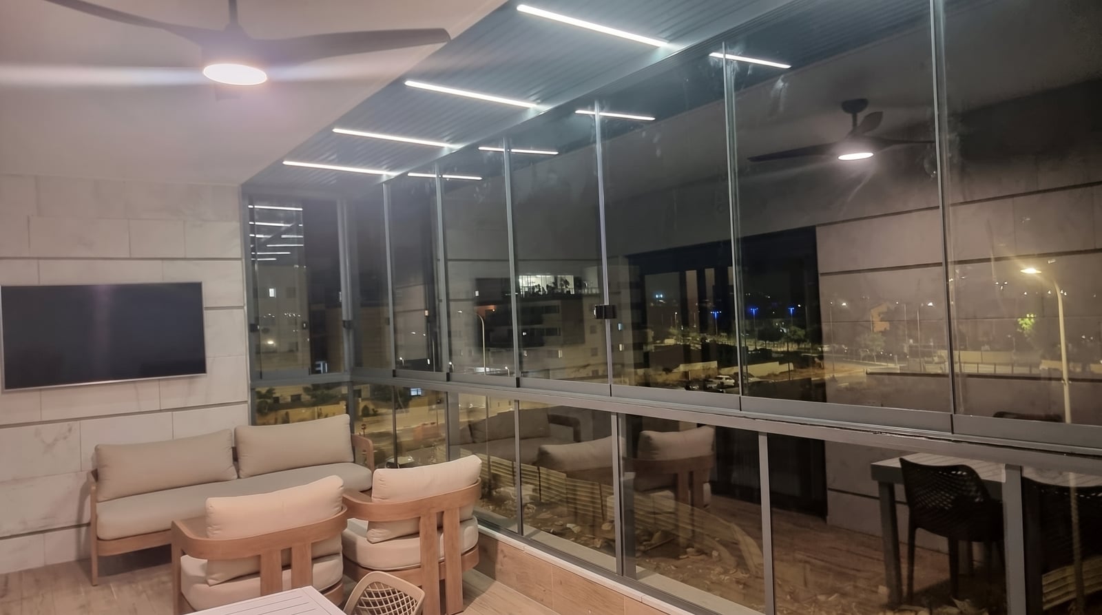 מרפסת סלון סגורה בזכוכית בלילה, ספה, טלוויזיה ומאוורר תקרה