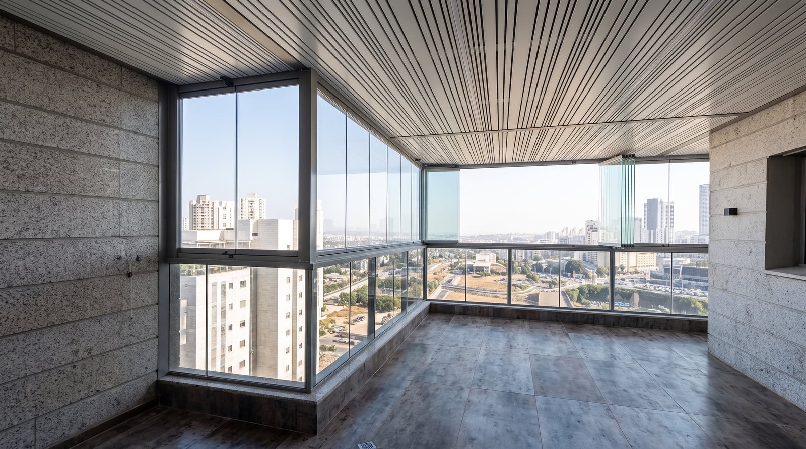 מרפסת פינתית רחבה סגורה בזכוכית עם תקרת אלומיניום מפוספסת ונוף עירוני