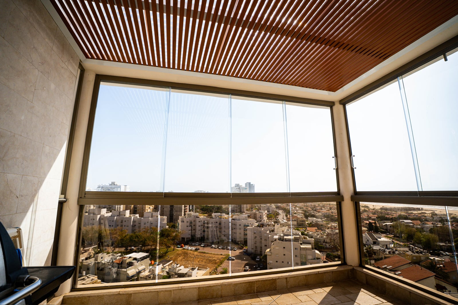 סגירת זכוכית למרפסת עם ידיות, פרגולה דמוי עץ ונוף לשכונה ולים