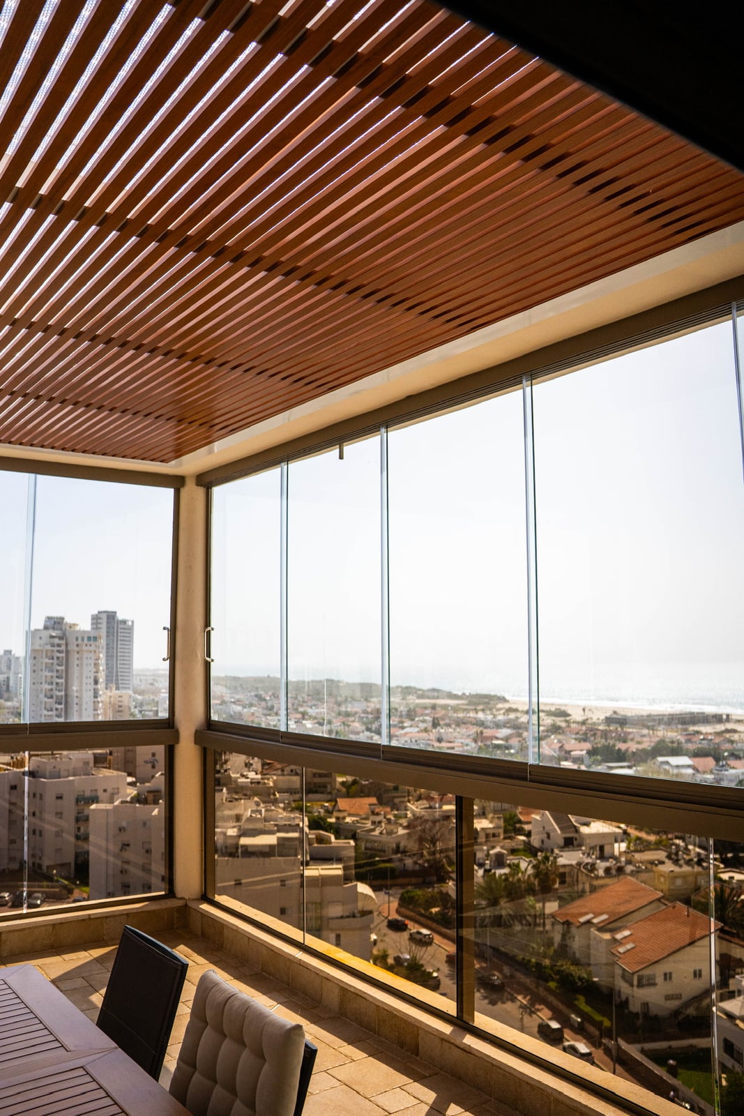 סגירת זכוכית לגובה מלא מתחת לפרגולה דמוי עץ, מבט לחוף ולשכונה