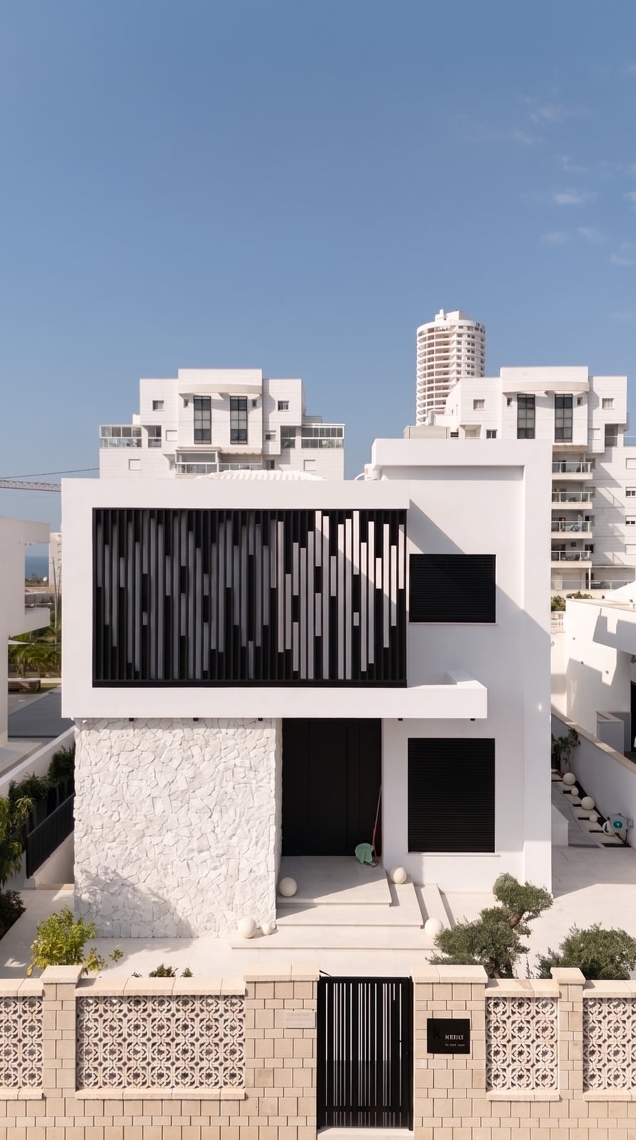 בית לבן עם לוברים אנכיים שחורים בקומה העליונה, חומת בלוקים ושער שחור
