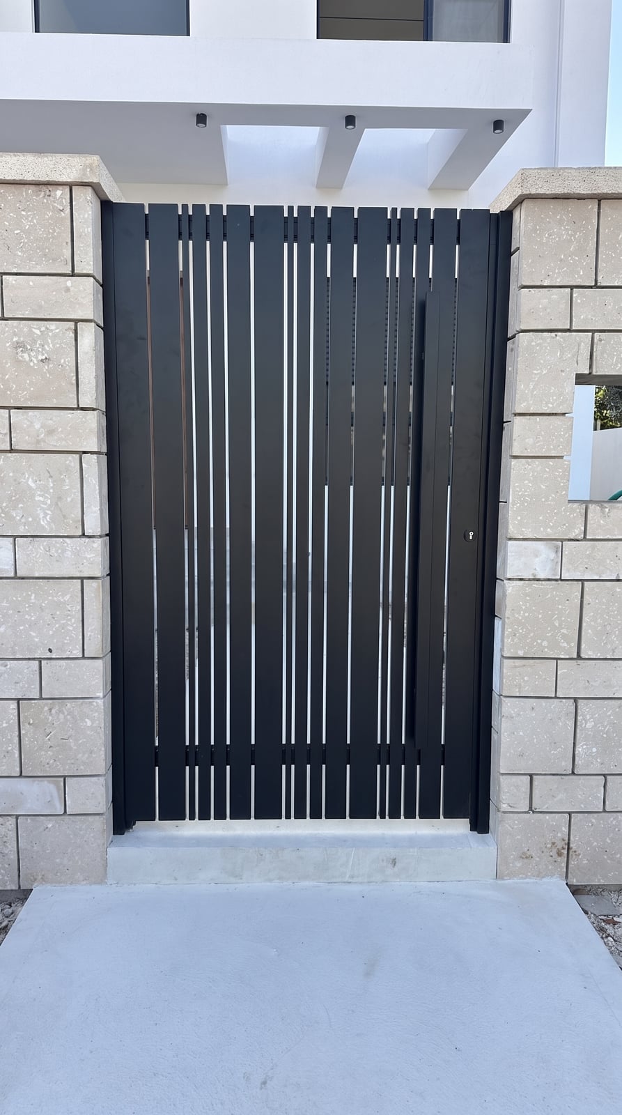 שער הולכי רגל שחור בשלבים אנכיים ברוחב משתנה בין עמודי אבן