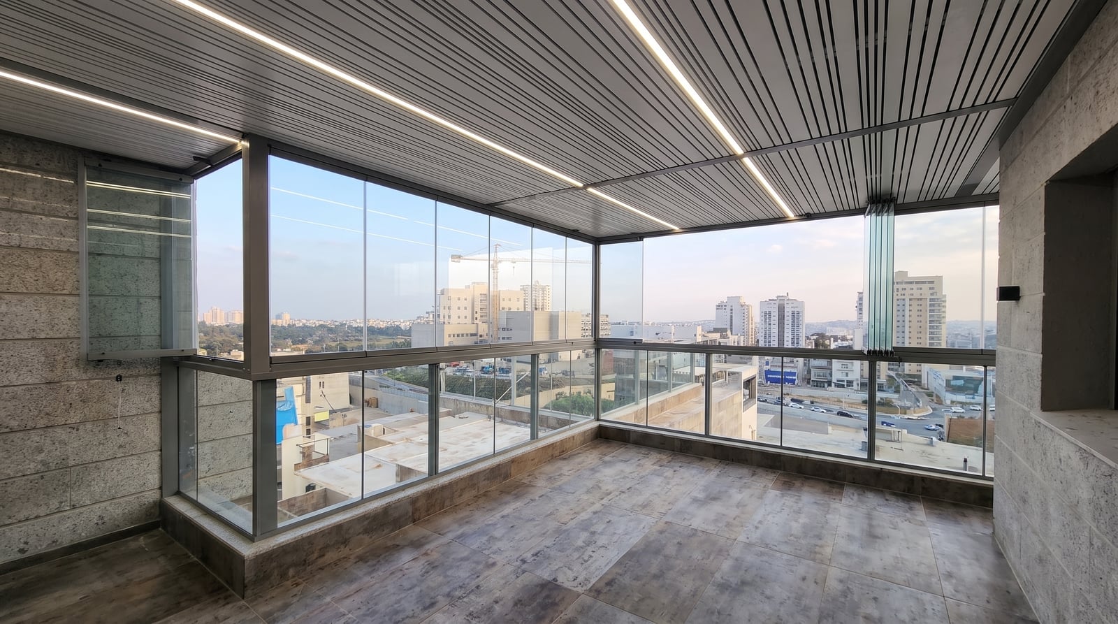 מרפסת עם סגירת זכוכית מתקפלת ותקרת לוברים אפורה עם פסי לד