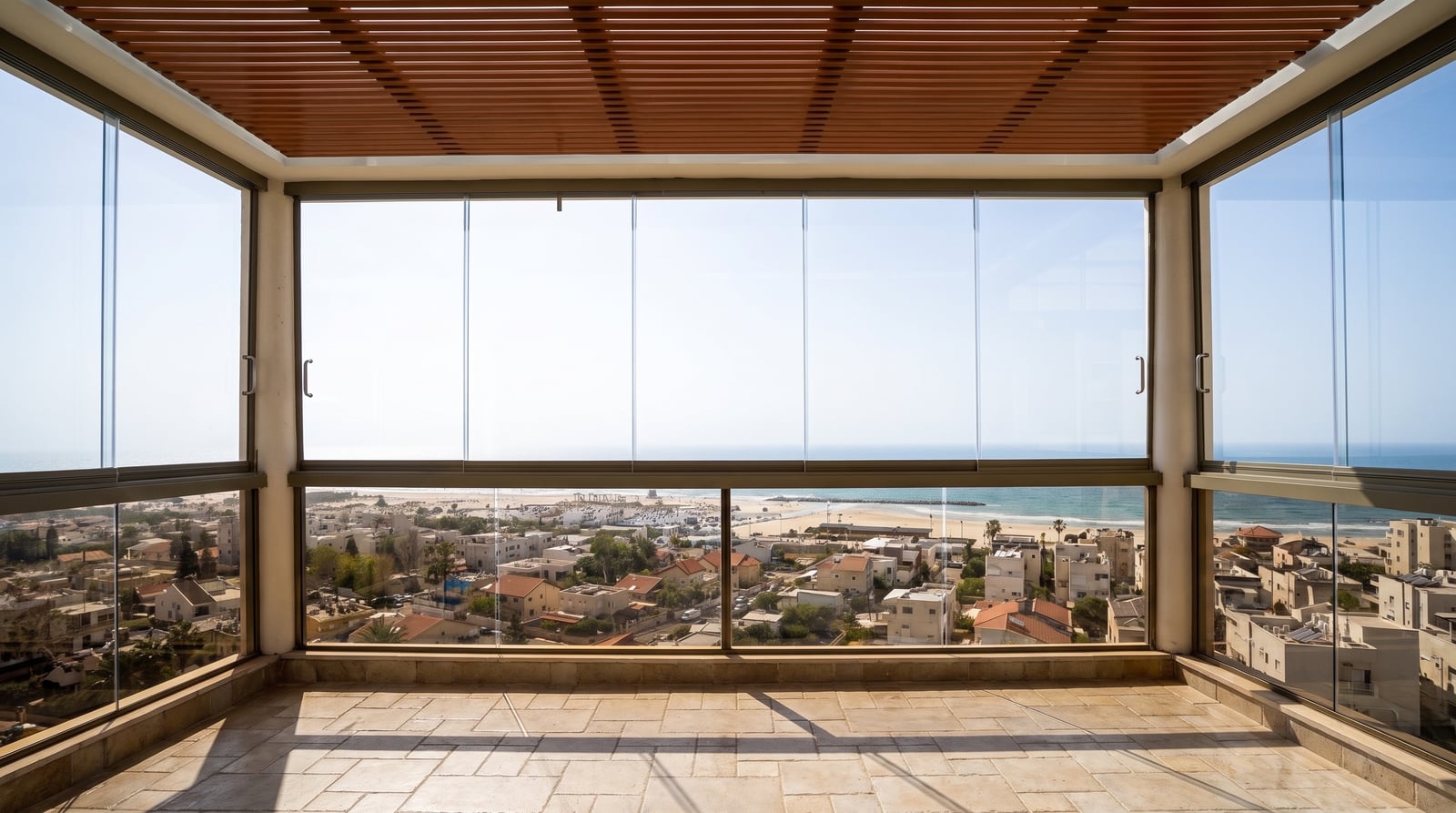 מרפסת עם סגירת זכוכית ותקרת פרגולה בגוון עץ, נוף לים
