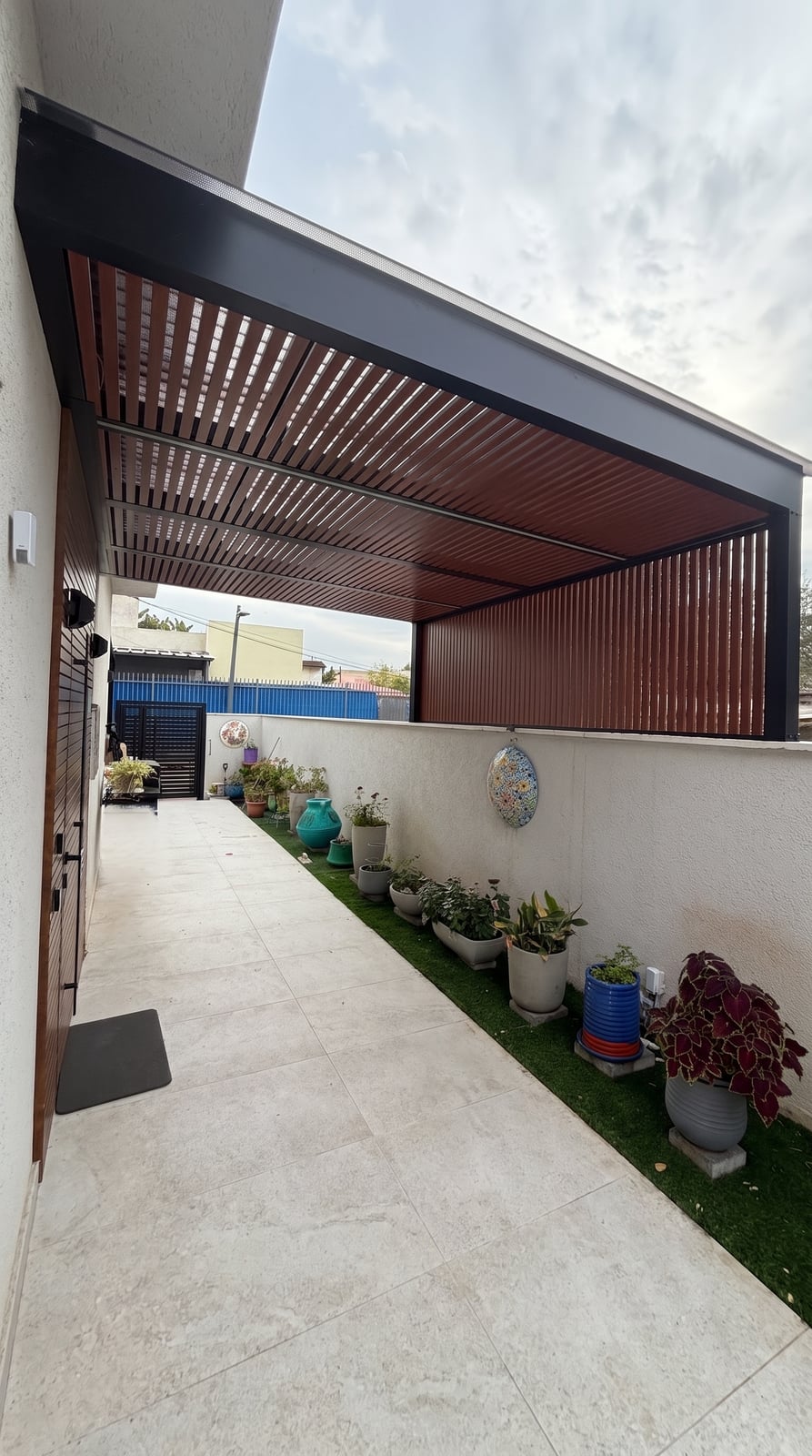 פרגולה שחורה עם שלבים בגוון עץ ומחיצה צדדית מעל שביל צדדי ליד הבית