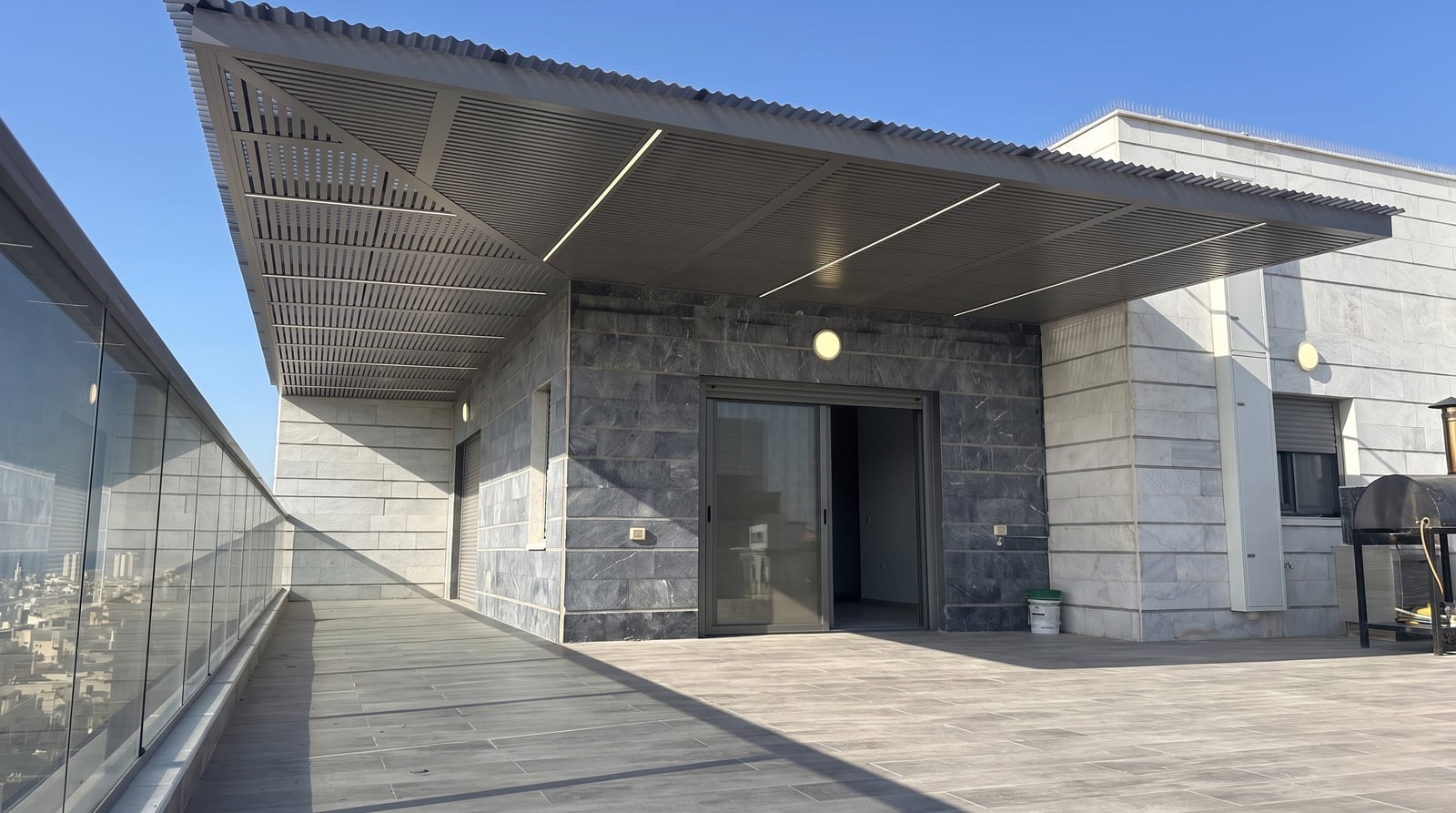 פרגולה אפורה כהה עם שלבים ופסי לד במרפסת גג עם מעקה זכוכית