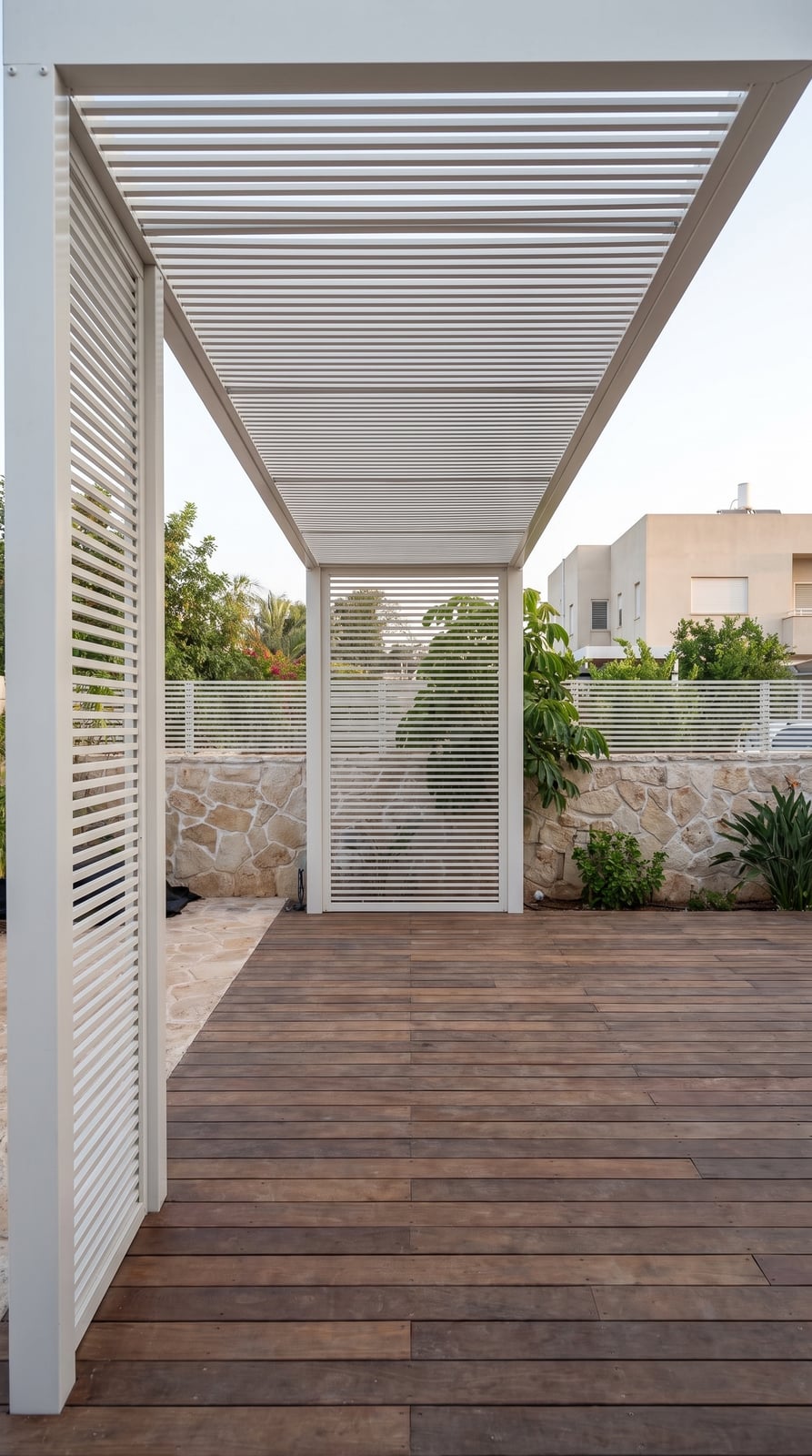 פרגולת אלומיניום לבנה עם מחיצות רפפות לבנות מעל דק עץ בגינה