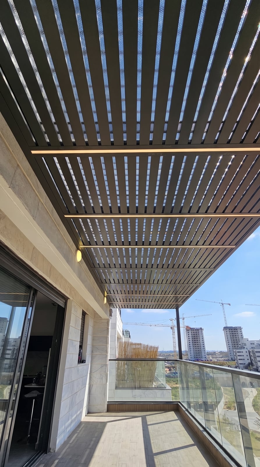 פרגולת אלומיניום אפורה כהה עם פסי לד במרפסת קומה גבוהה עם מעקה זכוכית