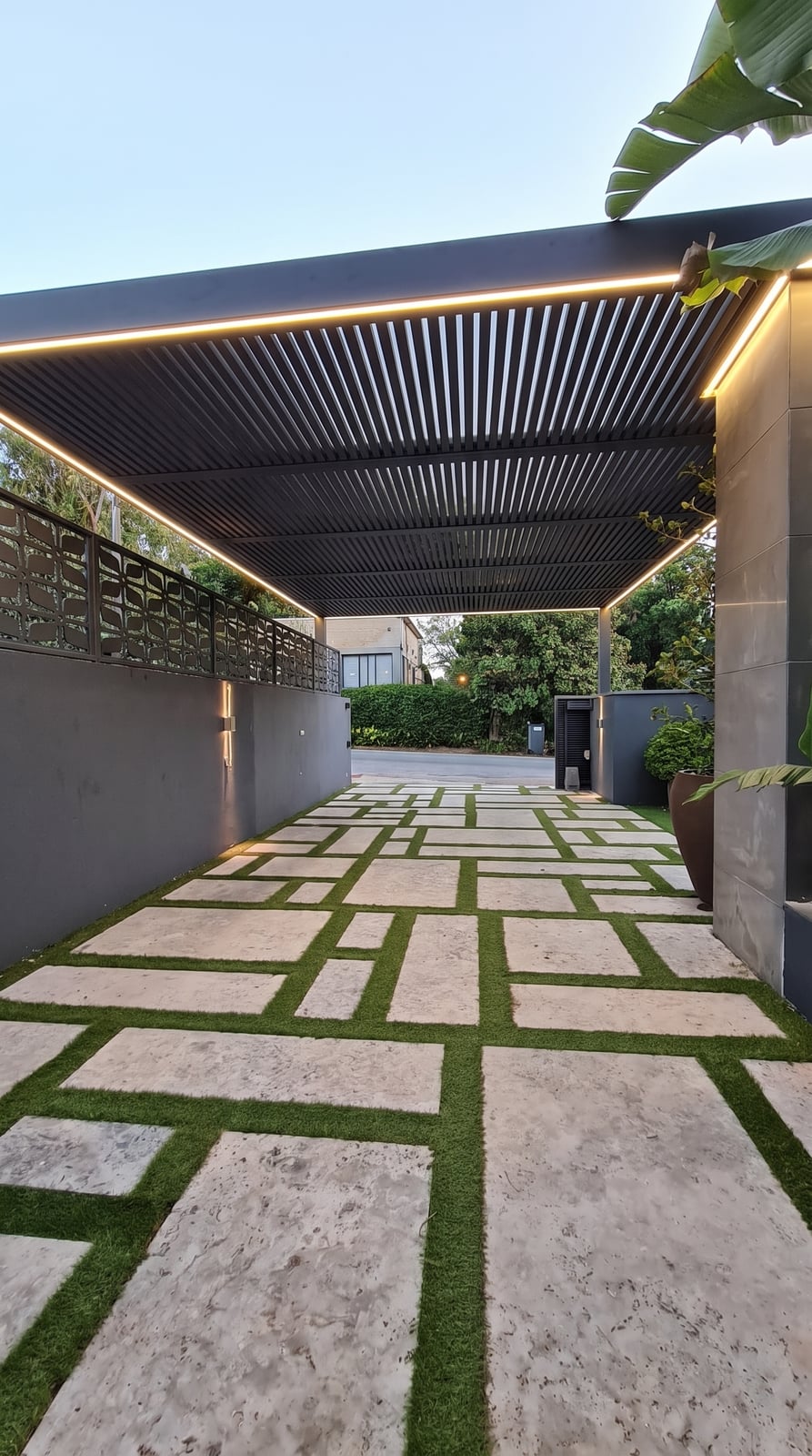 פרגולה אנתרציט עם תאורת לד היקפית מעל שביל כניסה מרוצף ודשא