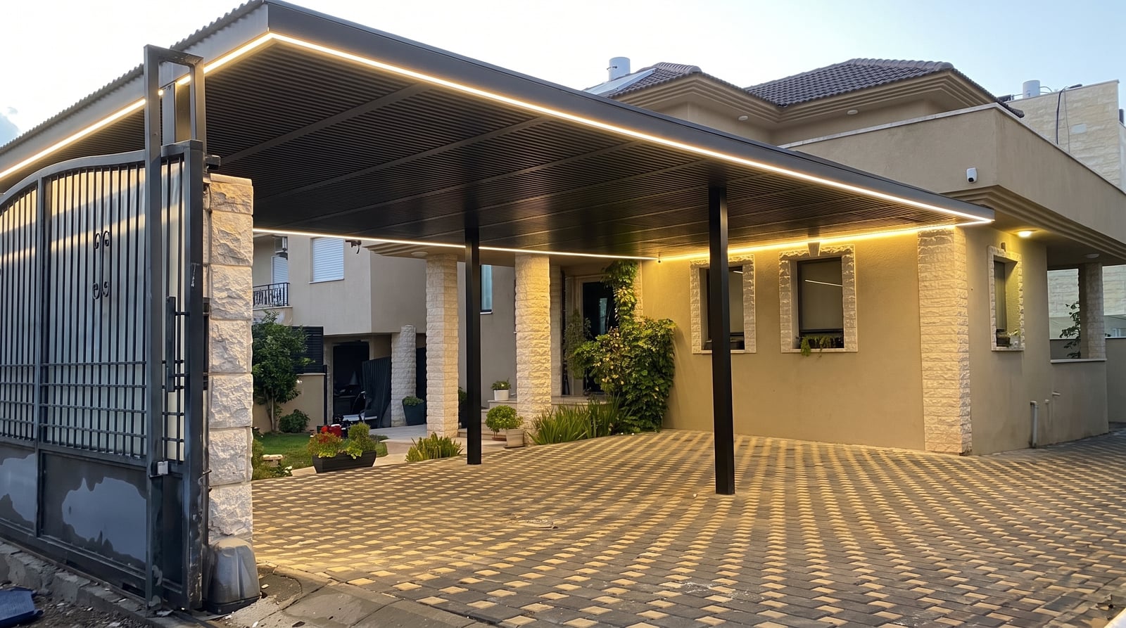 פרגולה כהה עם תאורת לד היקפית מעל חניה מרוצפת בכניסה לבית